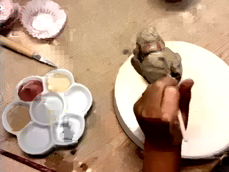 Kind bemalt eine getöpferte Tonfigur am Arbeitstisch der Kunsttruhe Magdeburg, daneben Farbpalette und Werkzeug