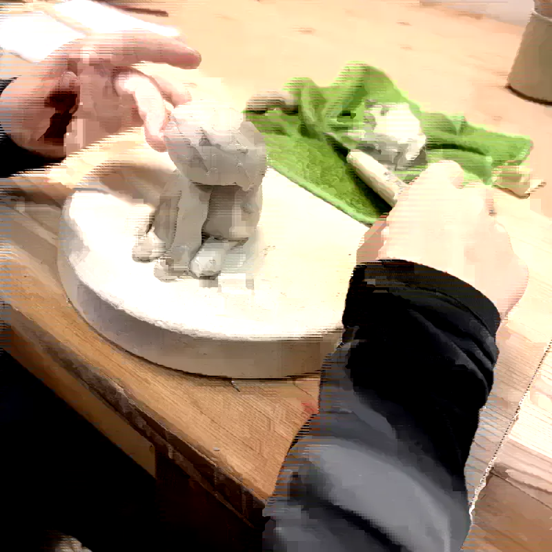 Kinderhände formen eine sitzende Tierfigur aus Ton auf einer Gipsplatte in der Kunsttruhe Magdeburg