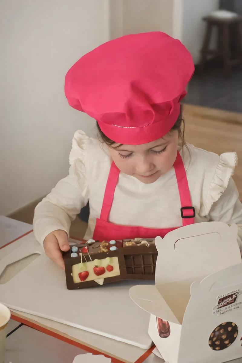 Kind mit pinker Kochmütze und selbst gestalteter Schokolade im FERI Chocolate Studio